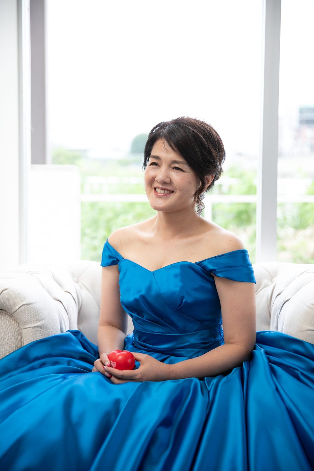 大きな窓の前の椅子に腰かけるブルードレスの女性